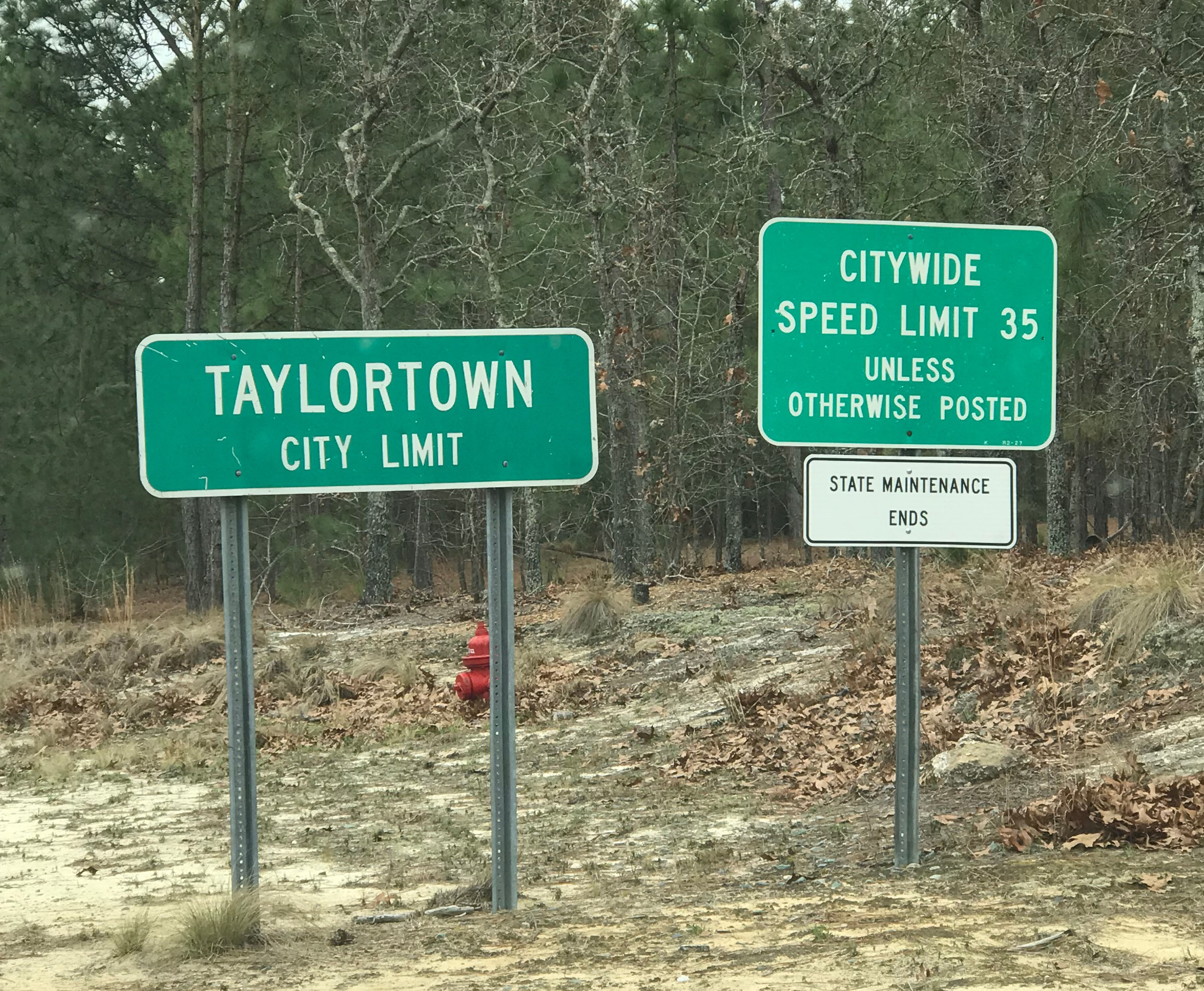Two signs are shown along the side of the highway. One reads "Taylortown, City Limit" and the other reads "Citywide Speed Limit 35; Unless Otherwise Posted; State Maintenance Ends"