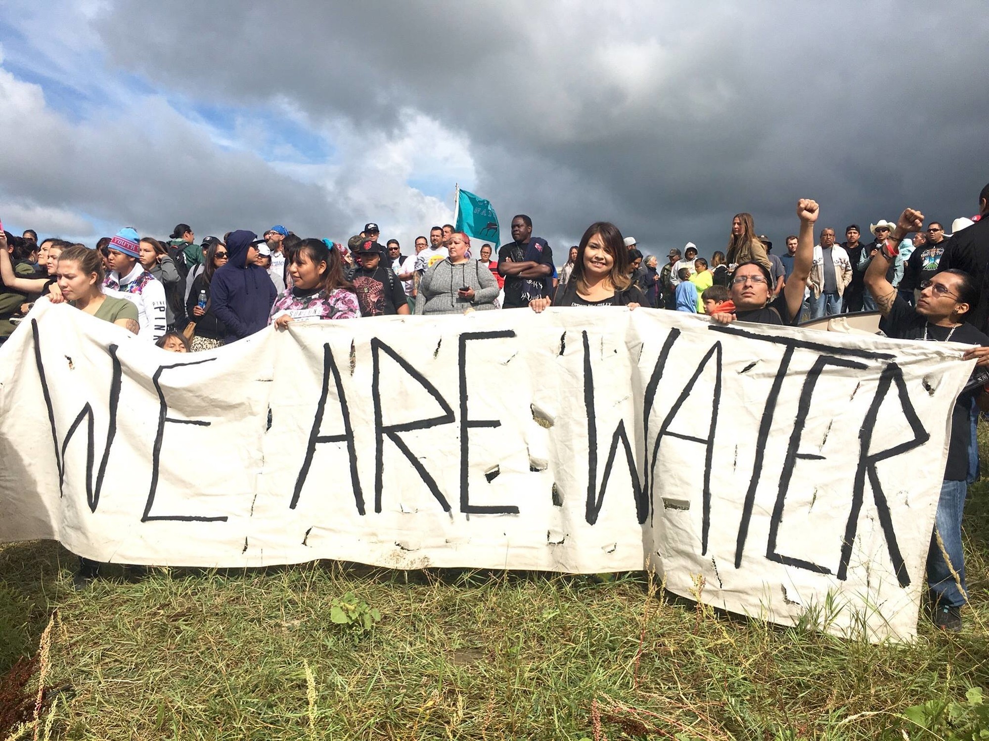 A large group of Alaskans hold a "WE ARE WATER" banner as part of a Stand With Standing Rock #NoDAPL protest in 2016