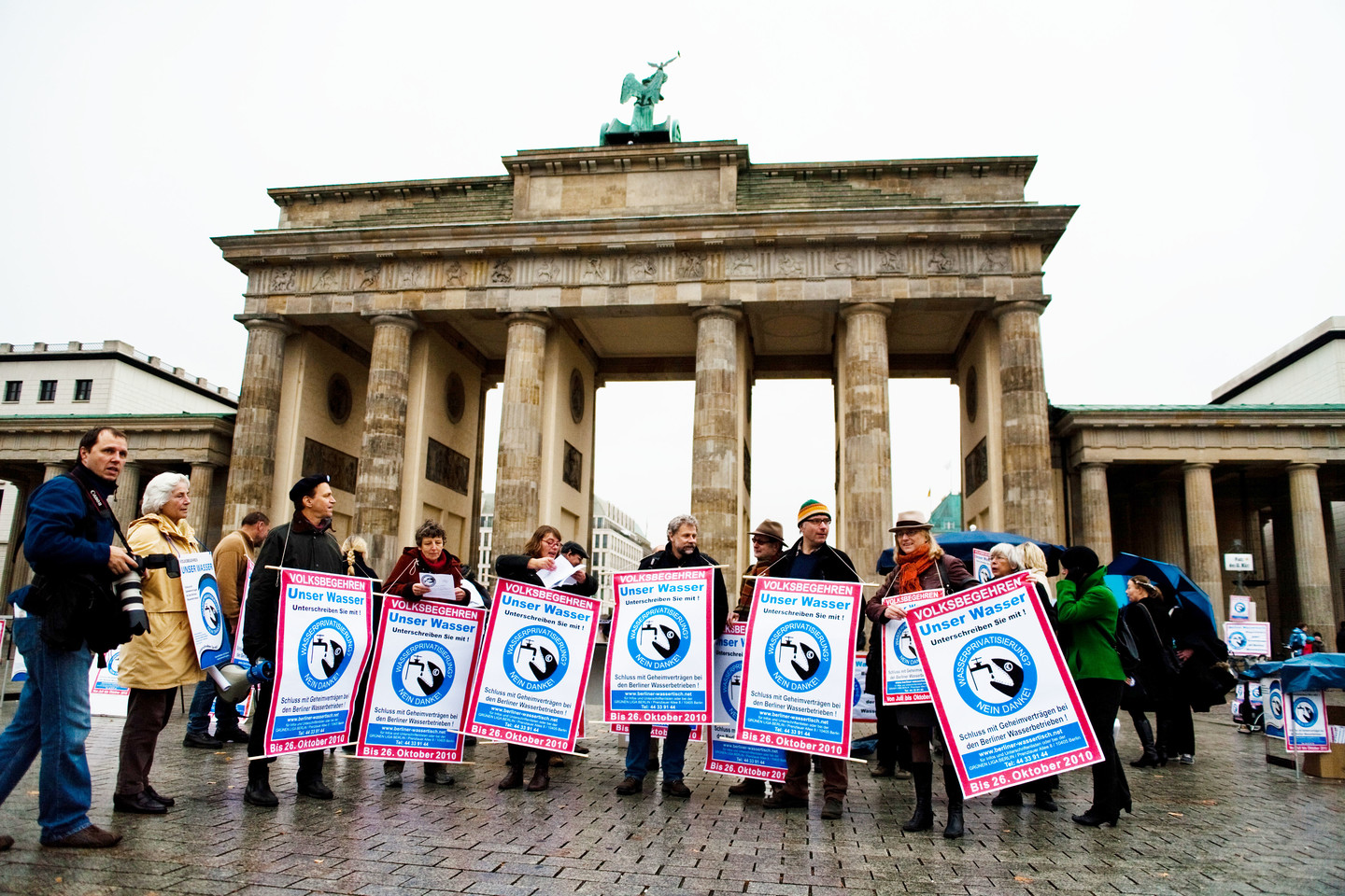 A group of water activists stand in front of the Brandenburger Tor holding protest signs.