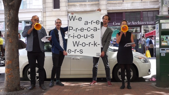 Members of The Architecture Lobby performance, holding a sign that reads, "We are Precarious Workers," outside the National AIA Convention in 2016