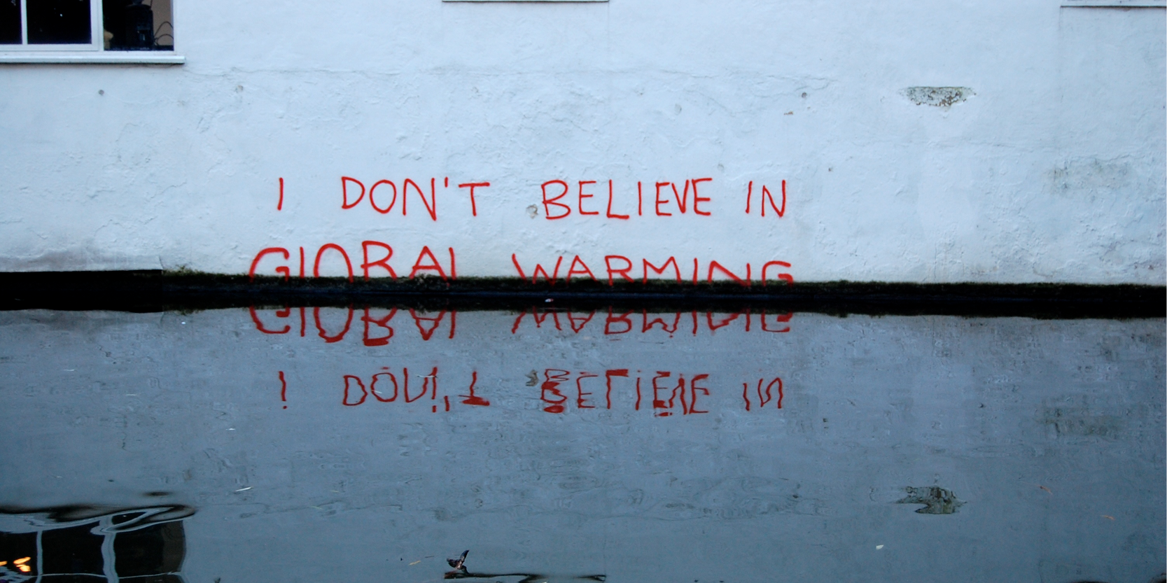 "I don't believe in Global Warming" written in spray paint reflected in flooded groundwater