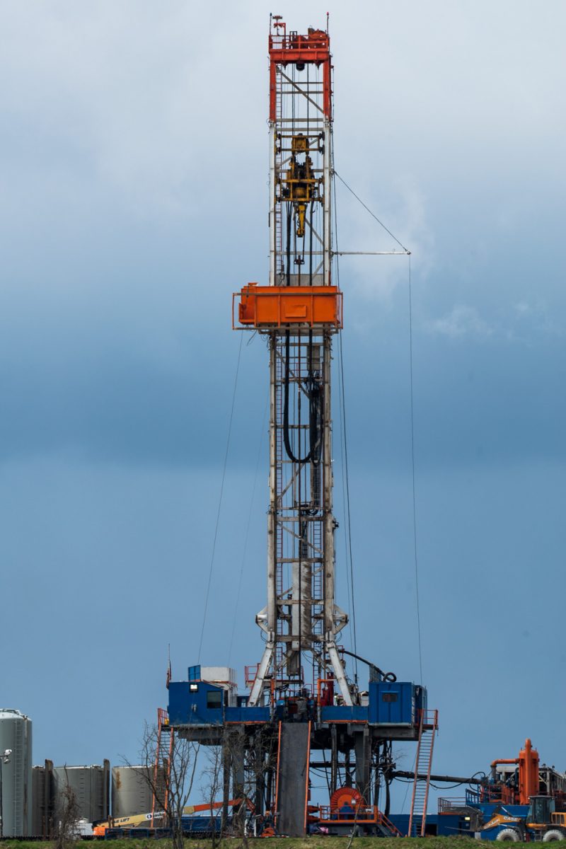 A tall metal fracking rig rises against a gray-blue sky