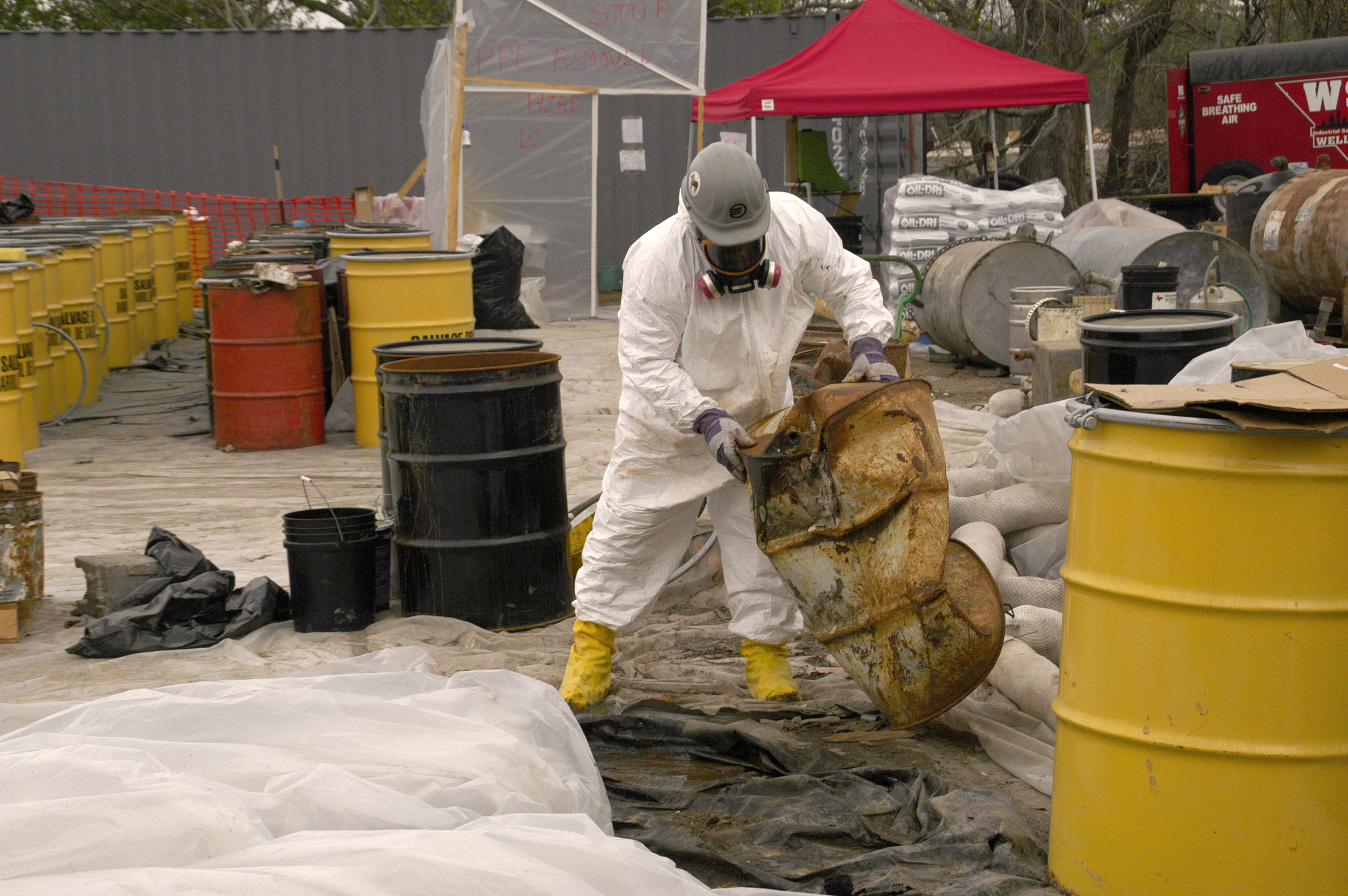 A worker in hazmat suit checks a potentially hazardous barrel to determine its contents