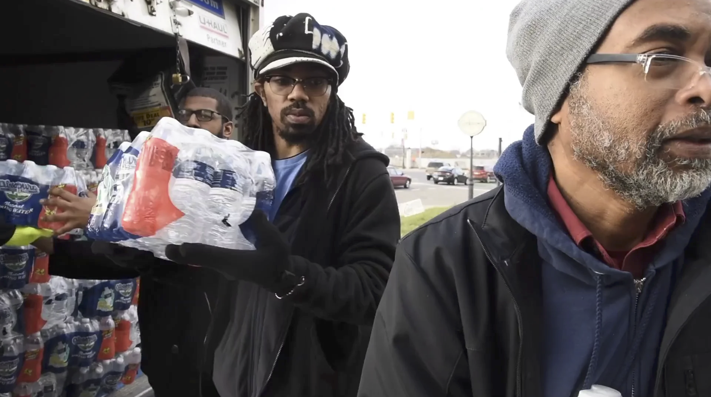 Dennis Black, B. Anthony Holley, and Kim Hunter unload water at the We the People of Detroit water station at St. Peter’s Episcopal. Film still from Kate Levy, Detroit’s Water Affordability Crisis, 2017.