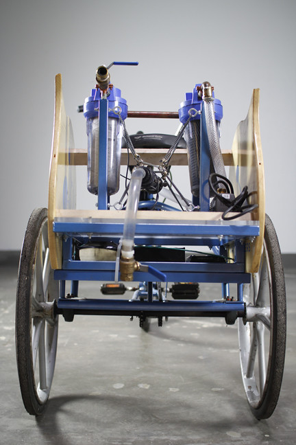 Front view of a blue tricycle with two front wheels, pipes, and filter systems