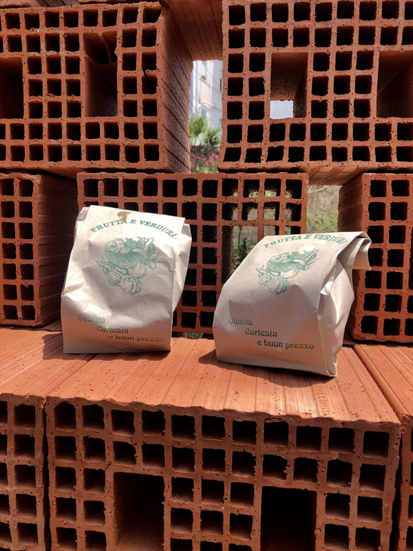 Two brown paper bags with labels sit on top of terra cotta bricks with cutouts, with more bricks stacked behind them.