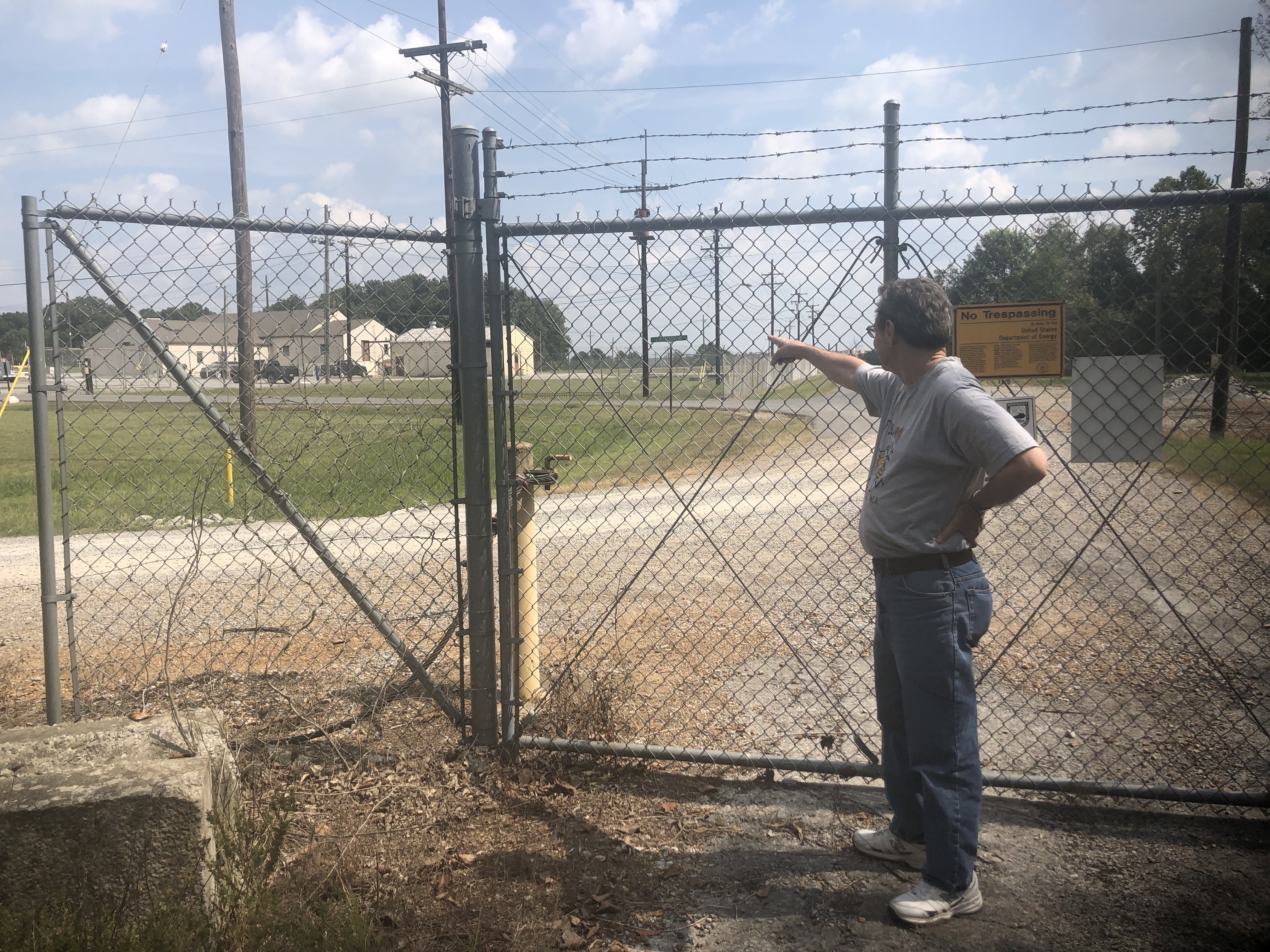 Greg Landhorff, former utilities worker at the Paducah Gaseous Diffusion Plant, stand in the West Kentucky Wildlife Management Area. He is pointing and looking through the fence line at the water treatment center where he used to work.