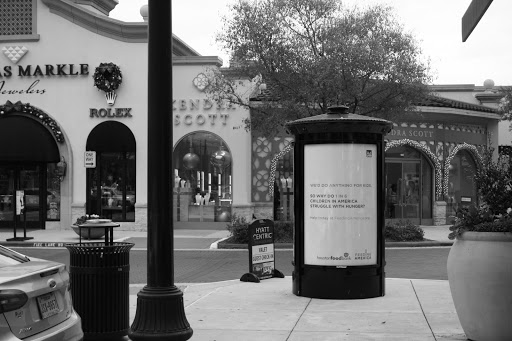 A black-and-white photo of an outdoor mall, with a sign that reads "We'd do anything for kids. So why do 1 in 6 children in America struggle with hunger?"