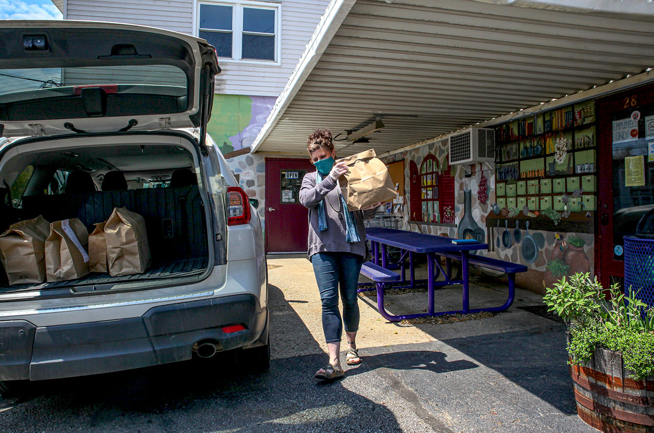 Carrie Tidd—co-owner of The Farmacy Natural and Specialty Foods grocery and deli in Athens, Ohio—loads delivery orders into a hatchback SUV while wearing a surgical mask