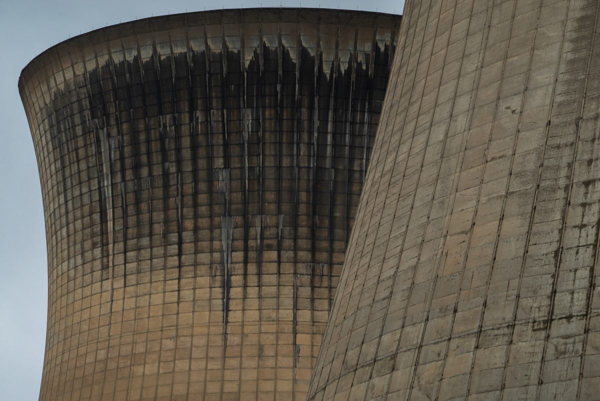 A closeup shot of two concrete cooling towers against a gray sky. One tower has significant soot soiling on its shell