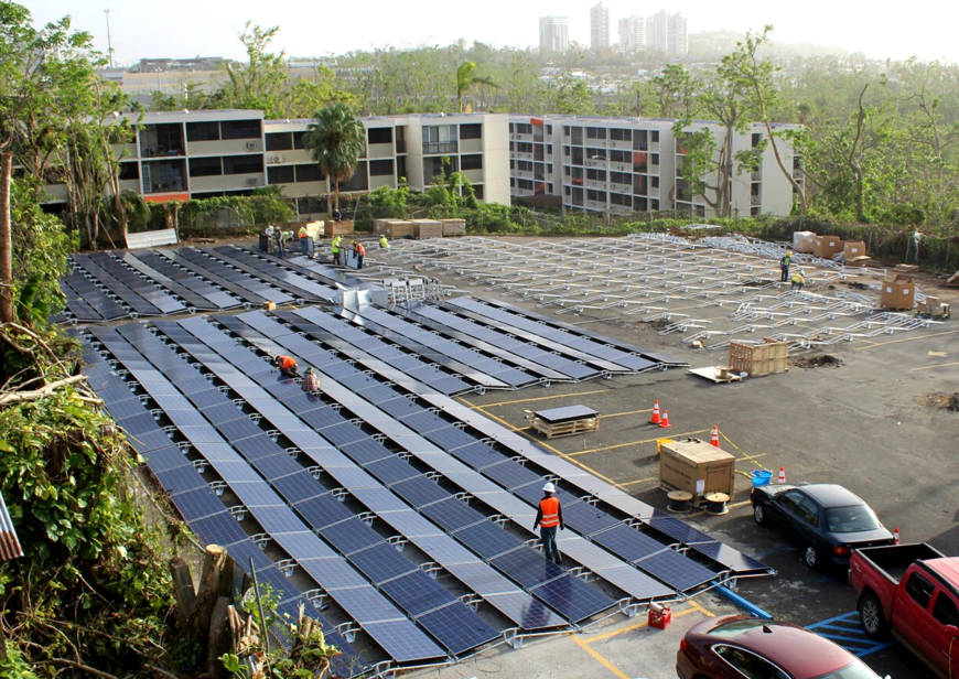 Image taken from outside a window of a building showing Installation of solar panels and battery units at a children's hospital in what used to be a parking lot