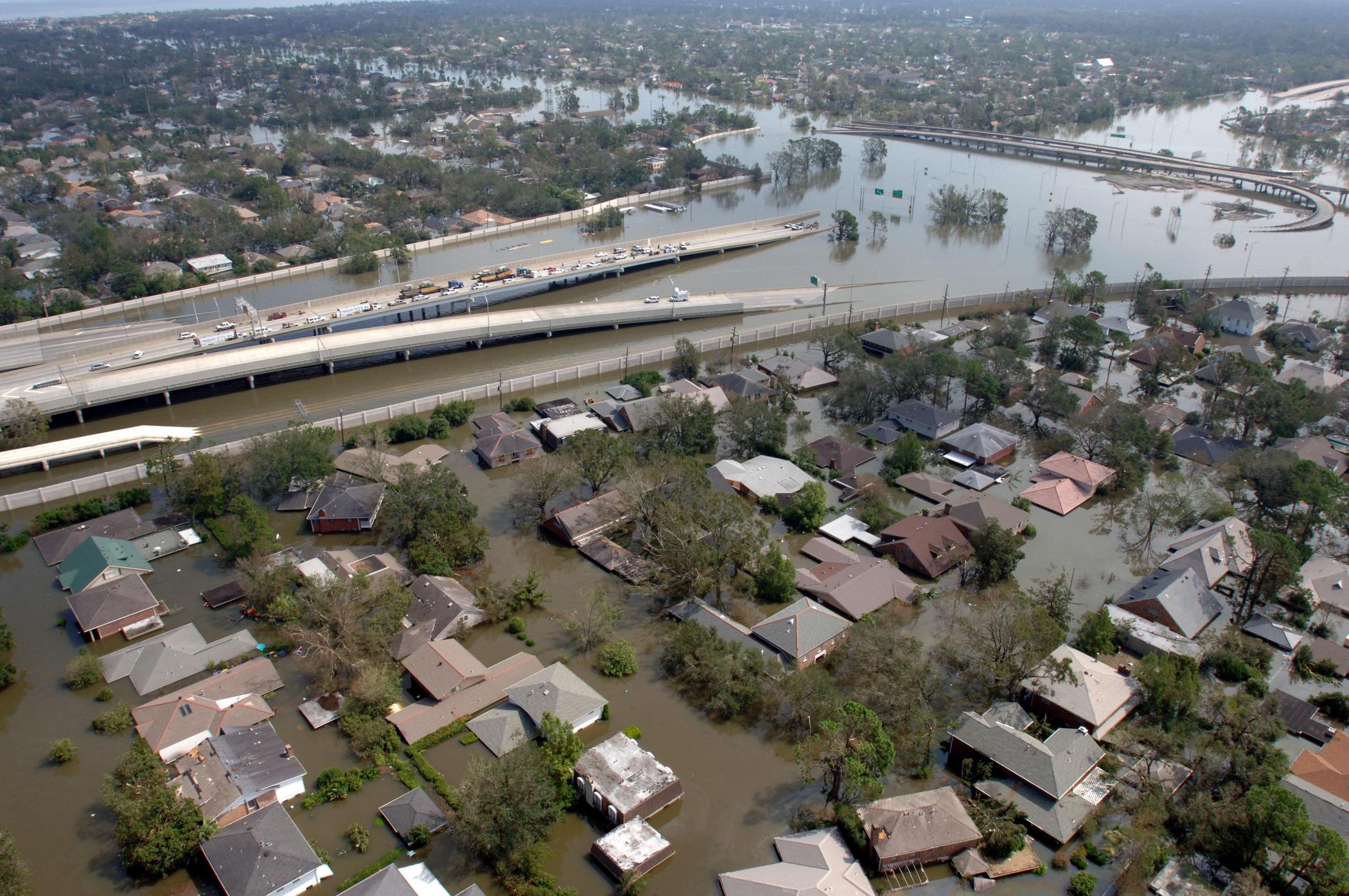Flooded houses and highway, with flyover bridges emerging from floodwaters, shown from above, horizon in the distance