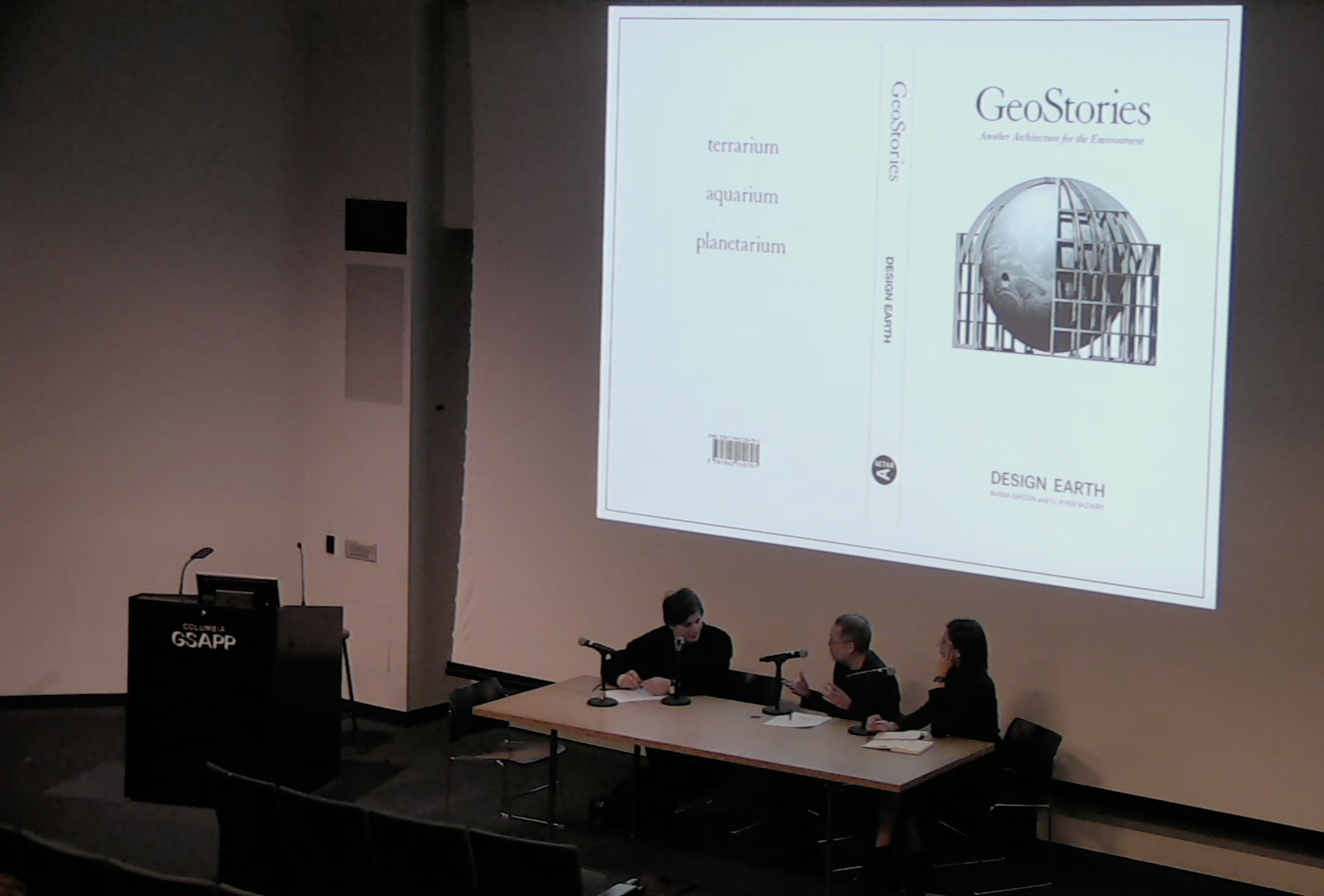Three people sit at a table with microphones in front of a large screen that shows the cover of a book titled "GeoStories"